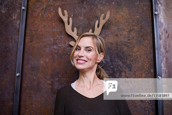 Portrait of mid adult woman  smiling  cardboard reindeer antlers on wall behind her