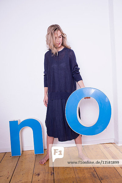 Portrait of mid adult woman  holding three-dimensional letter 'O'  next to letter 'N' on floor