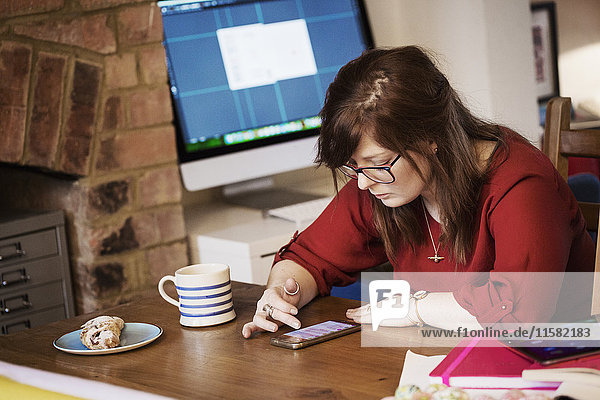 Eine junge Frau sitzt mit einer Tasse Kaffee und blättert ihre Nachrichten auf ihrem Smartphone durch.