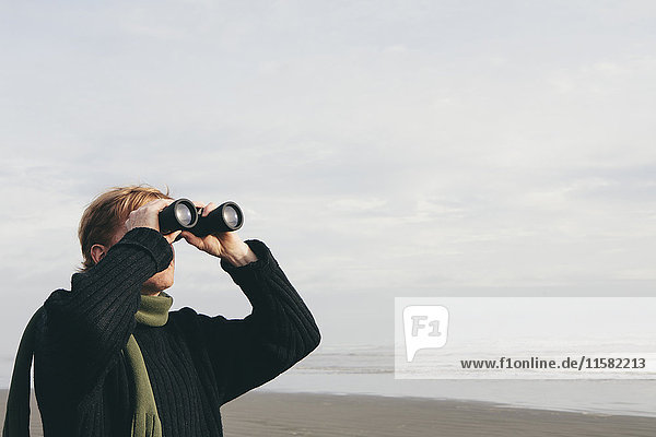 Middle aged man standing on a beach  looking through binoculars at Seabrook  Washington  USA.