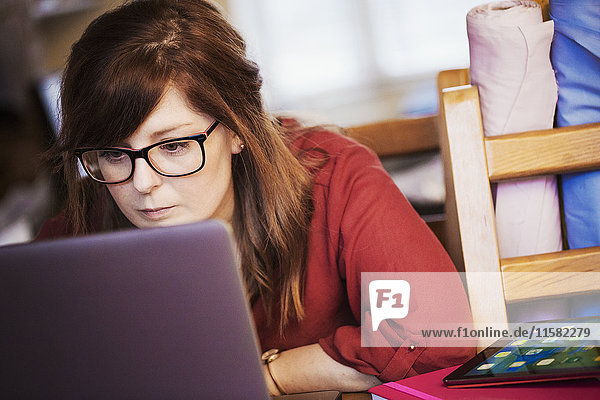 A young woman seated using her laptop leaning towards the screen to read content.