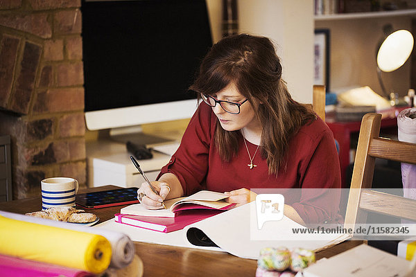 Eine Frau sitzt an einem Tisch  macht Notizen und schreibt in ein Notizbuch.