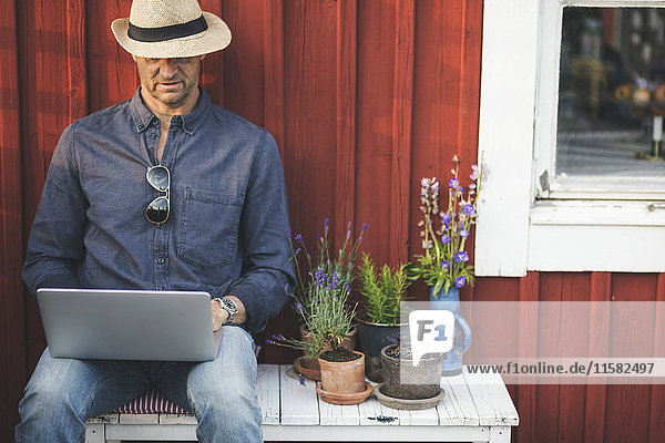 Mann mit Laptop auf der Bank bei Topfpflanzen im Hinterhof
