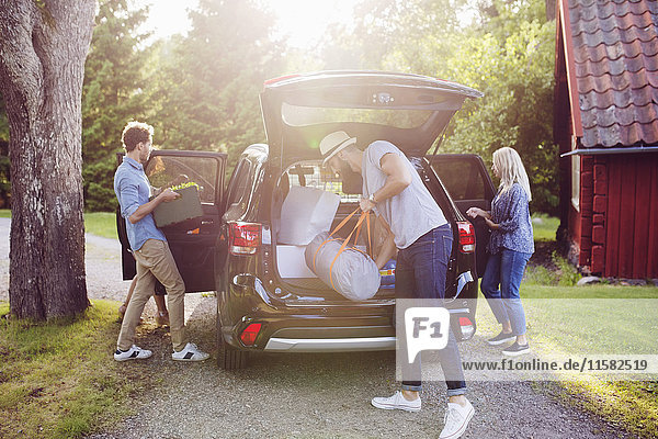 Full length of friends loading luggage into car on road during sunny day