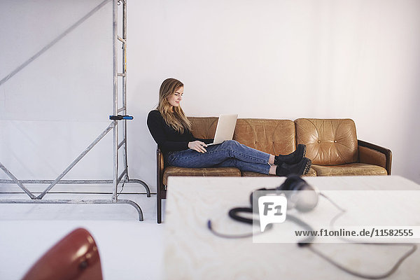Durchgehende Seitenansicht der jungen Frau auf dem Sofa im Büro mit Laptop