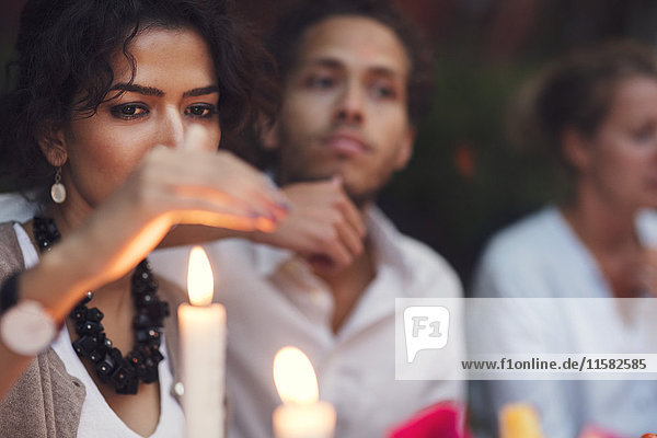 Woman covering candle while sitting with friends at garden party