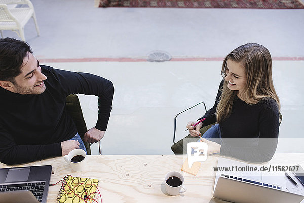 Hochwinkelansicht eines jungen Mannes und einer jungen Frau  die am Schreibtisch im Büro diskutieren.