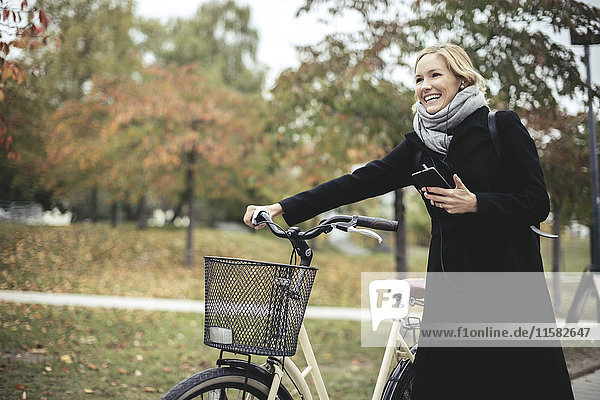 Smiling businesswoman enjoying music while walking with bicycle during autumn