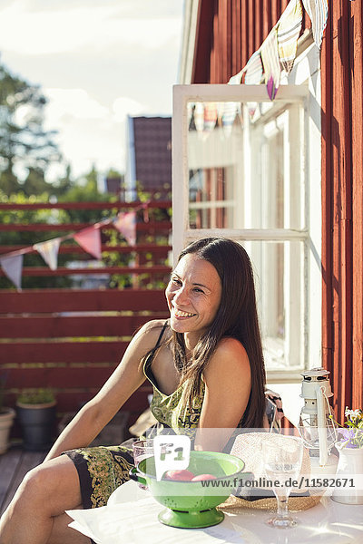 Fröhliche Frau am Tisch im Hinterhof an einem sonnigen Tag