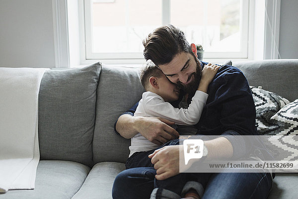 Vater umarmt den Sohn  während er zu Hause auf dem Sofa sitzt.