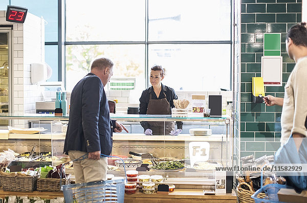 Mature man buying groceries from saleswoman in supermarket
