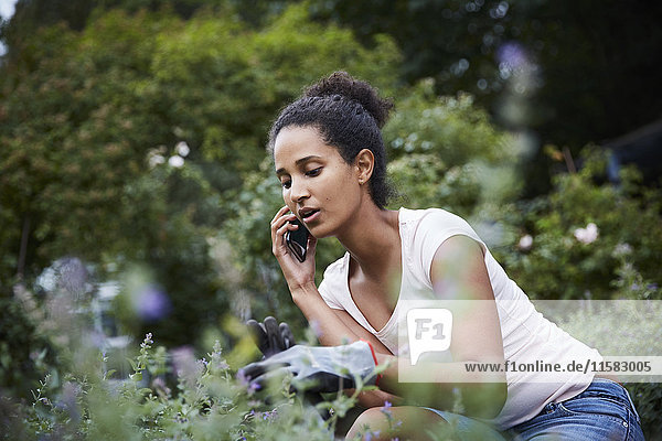 Young female gardener using mobile phone while looking at plants