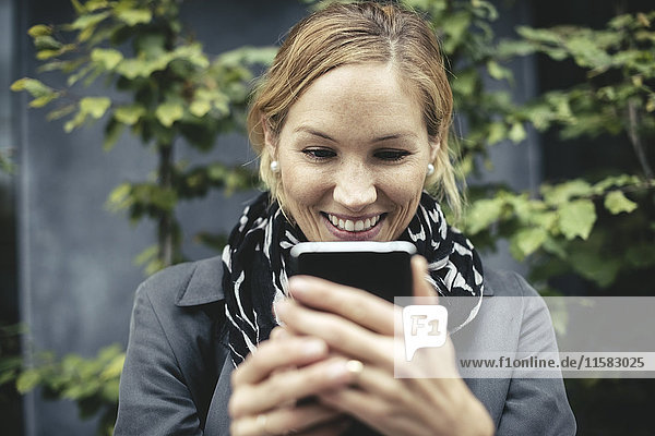 Smiling mid adult businesswoman using smart phone outdoors