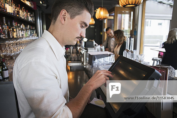 Side view of male owner using cash register at checkout in restaurant