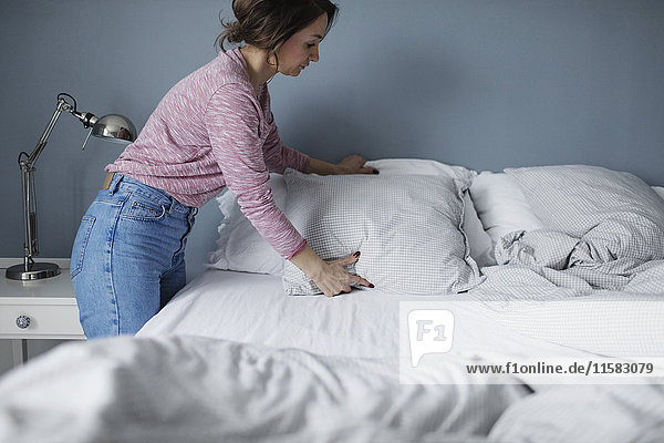 Seitenansicht der Frau  die die Kissen auf dem Bett zu Hause anordnet.