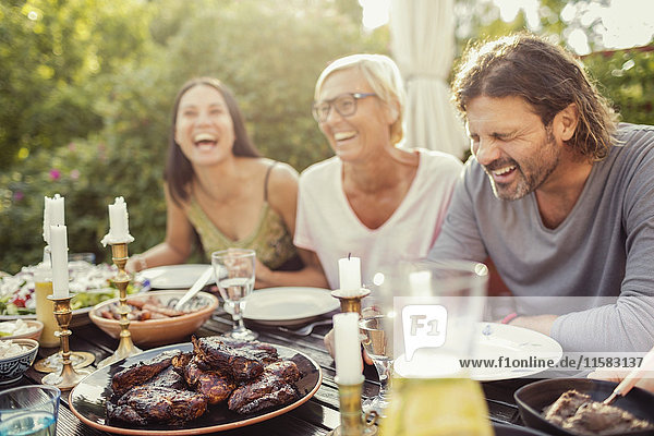 Fröhliches Paar und Freundin lachend auf dem Esstisch während der Gartenparty im Hinterhof