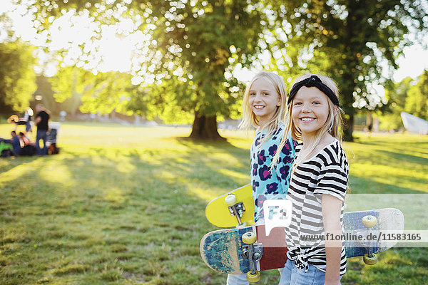 Portrait of smiling friends with skateboards at public park
