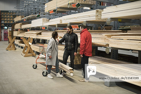 Kunden und Verkäufer stehen an Holzbrettern in den Regalen des Baumarktes.