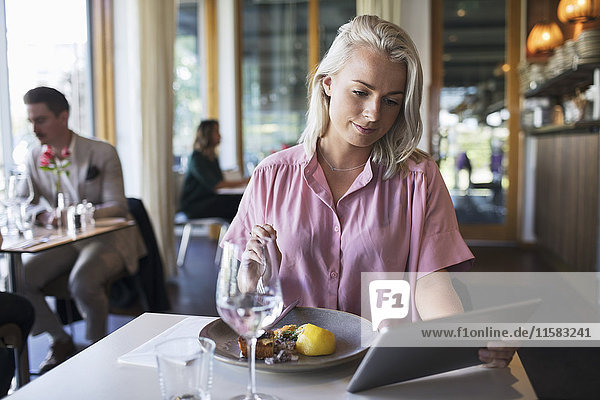 Junge blonde Geschäftsfrau beim Sitzen am Tisch im Restaurant mit digitalem Tablett