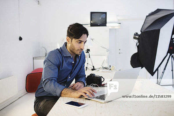 Male blogger using laptop at desk in creative office