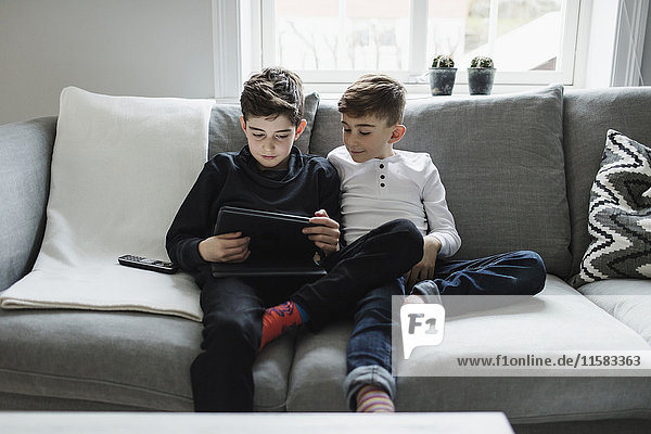 Boy looking at brother using digital tablet while sitting on sofa in living room