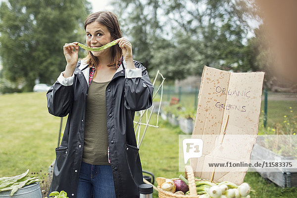 Lächelnde junge Frau zeigt frisch geerntetes Gemüse im Stadtgarten