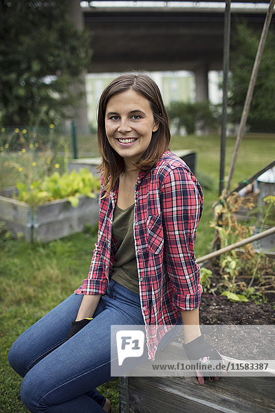 Porträt einer lächelnden erwachsenen Frau,  die auf einer Holzkiste im Stadtgarten sitzt.