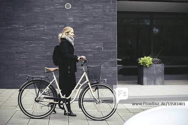Durchgehende Seitenansicht der mittleren erwachsenen Frau mit Fahrradspaziergang am Gebäude
