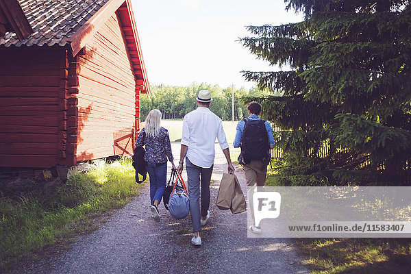 Rückansicht von Freunden mit Gepäck  die auf einem Wanderweg zwischen Hütten und Bäumen spazieren gehen.