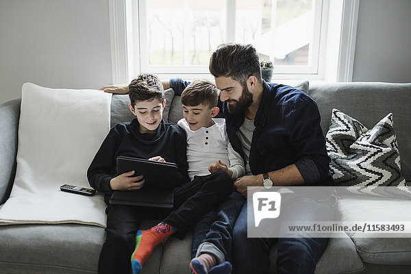 Vater und Sohn sehen den Jungen mit dem digitalen Tablett an  während er auf dem Sofa sitzt.