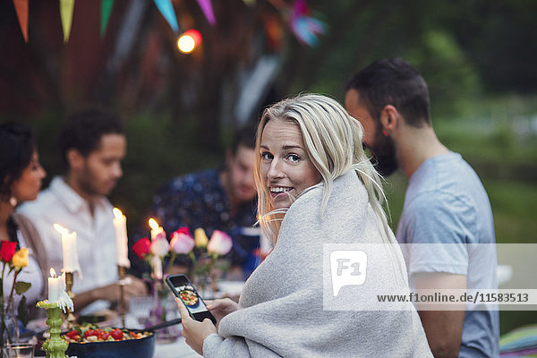 Porträt einer lächelnden Frau  die beim Sitzen mit Freunden auf der Gartenparty Essen fotografiert.