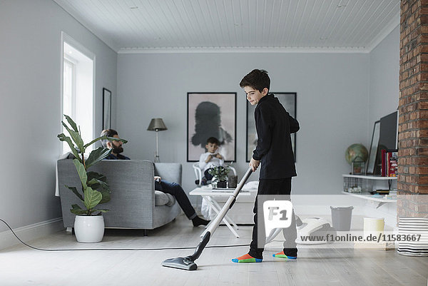 Boy vacuuming floor in living room at home