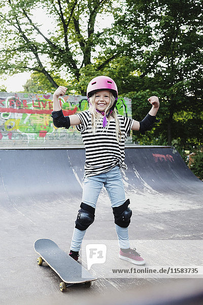 Lächelndes Mädchen  das auf der Skateboard-Rampe steht und seine Muskeln beugt.