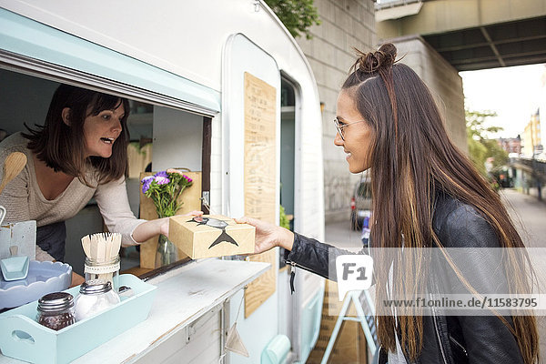 Side view of woman buying food from female owner at food truck