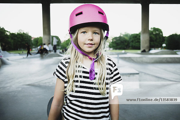 Porträt eines lächelnden Mädchens mit rosa Helm im Skateboardpark