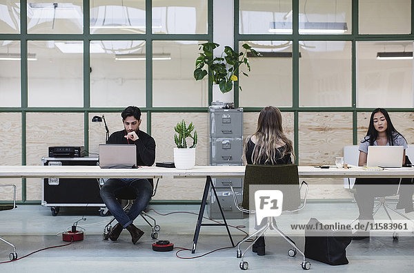Two women and one man working at desk in creative office