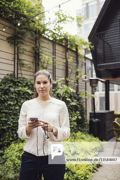 Portrait of confident businesswoman holding smart phone at office yard