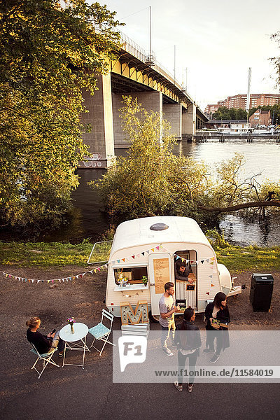 Hochwinkelansicht von Kunden und Food-Truck-Besitzer auf der Straße mit Brücke im Hintergrund