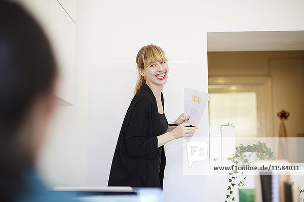 Lächelnde mittlere erwachsene Geschäftsfrau  die ein Dokument hält  während sie einen Kollegen im Büro anschaut.