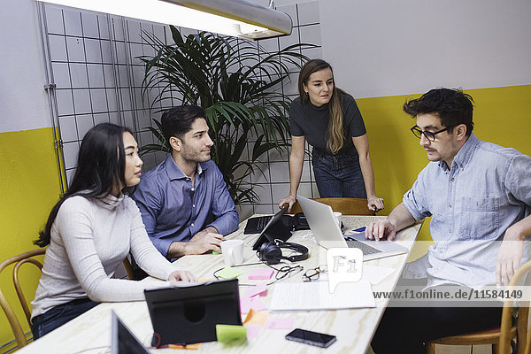 Kollegen  die ihren Kollegen bei der Besprechung im Büro mit dem Laptop anschauen