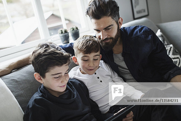 Neigungsaufnahme von Vater und Sohn  die den Jungen mit einem digitalen Tablett im Wohnzimmer betrachten.