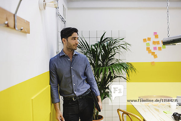 Thoughtful young man leaning on wall in creative office