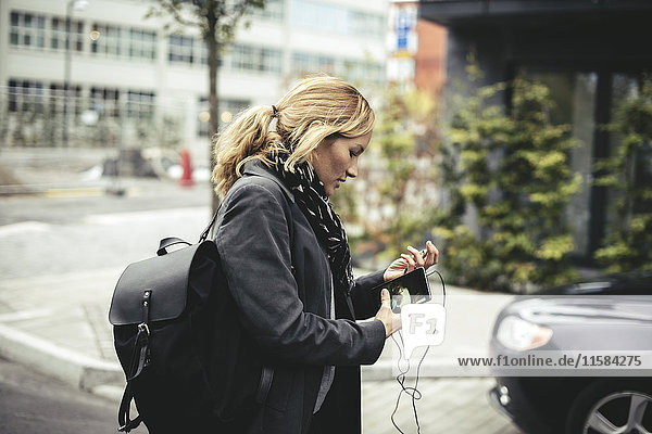 Seitenansicht der mittleren erwachsenen Geschäftsfrau  die ein Smartphone hält  während sie auf der Stadtstraße spazieren geht.