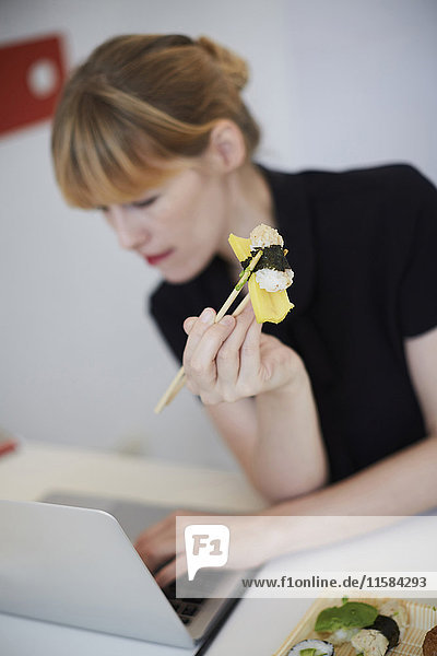 Geschäftsfrau mit Sushi bei der Nutzung des Laptops am Tisch im Büro