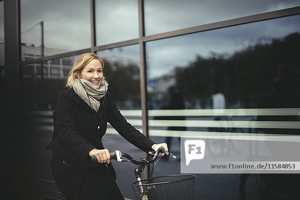 Smiling mid adult businesswoman riding bicycle by city building