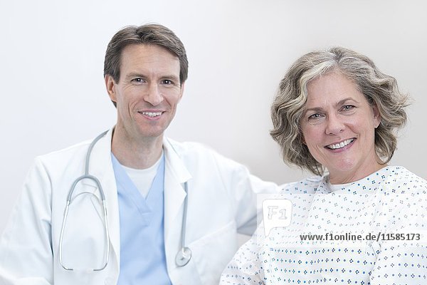 Männlicher Arzt und weibliche Patientin lächeln in Richtung Kamera.