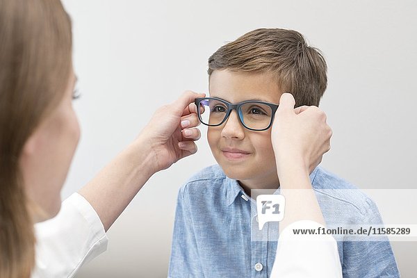 Eine Optikerin setzt einem Jungen eine Brille auf.