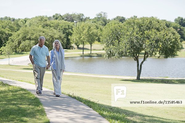 Älteres Paar  das auf einem Weg im Park am See spazieren geht.