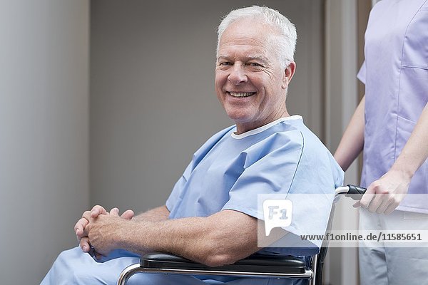 Älterer Mann im Krankenhauskittel im Rollstuhl  lächelnd.