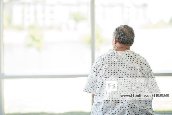 Männlicher Patient im Kittel schaut durch ein Krankenhausfenster  Rückansicht.